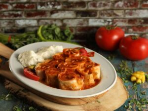 Prato branco com rolinhos de massa recheada em molho vermelho, molho branco, tomate e pepino