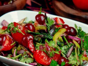 Salada colorida com tomates, cerejas, cebola roxa e folhas verdes em travessa branca