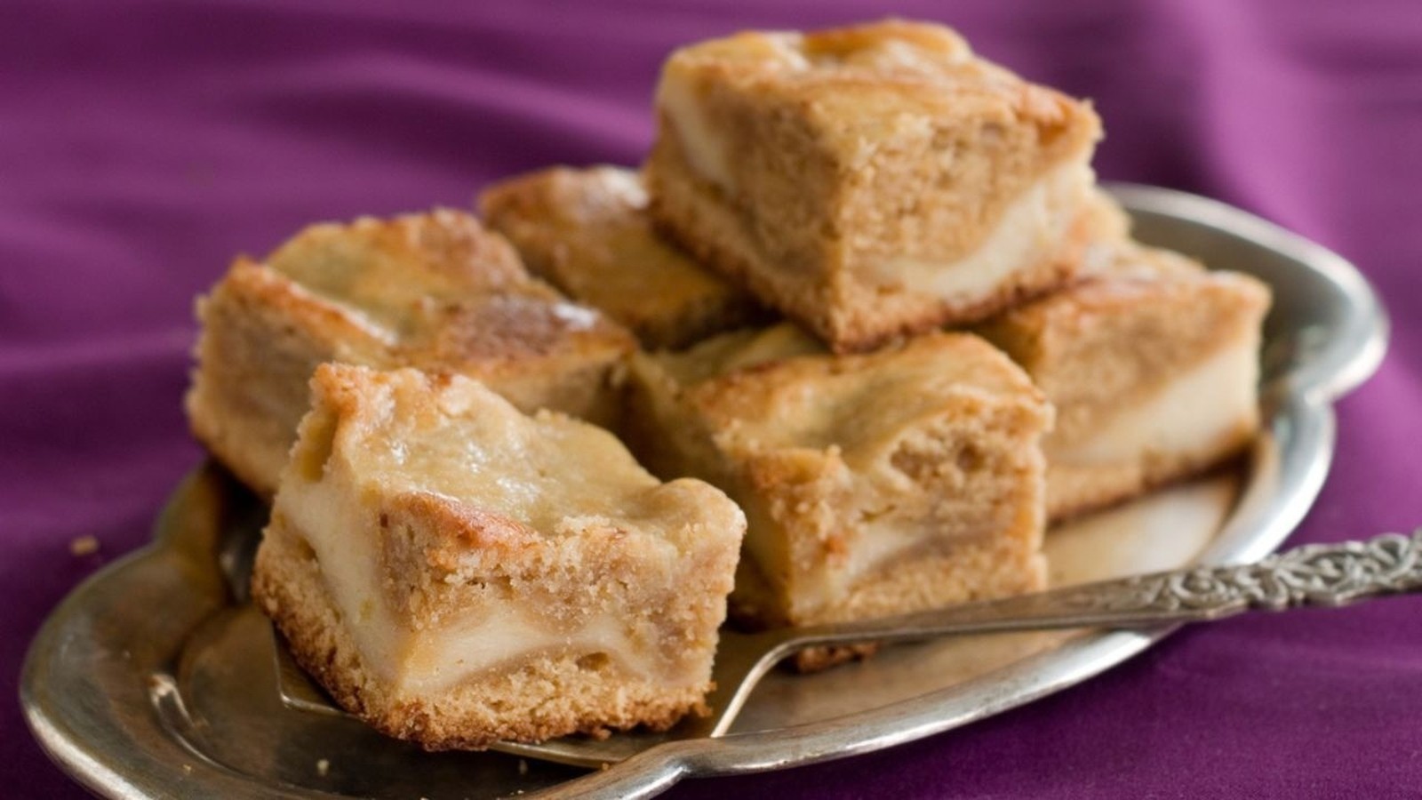 Múltiplos blondies de chocolate branco em um prato prateado sobre um fundo roxo