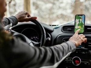 Pessoa no carro, mãos no volante e no celular com aplicativo de mapa, painel, 22.0c