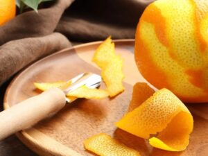 Laranja parcialmente descascada, cascas de laranja e zester de cabo de madeira em tábua