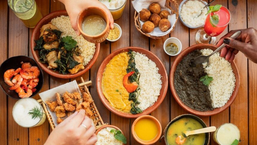 Mesa de madeira com diversos pratos típicos paraenses: maniçoba, camarão, arroz, caldo e bebidas