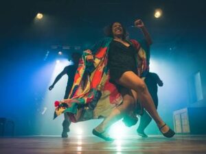 Mulher dançando com roupão colorido em palco iluminado por luzes azuis durante performance