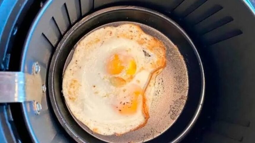 Dois ovos fritos em uma pequena frigideira redonda dentro da cesta preta de uma airfryer