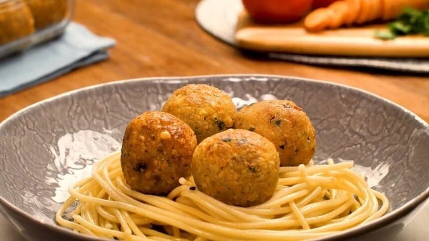 Prato cinza com espaguete e quatro almôndegas redondas e douradas, com fundo desfocado