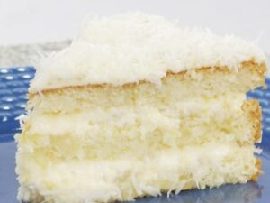 Fatia de bolo gelado com camadas de massa clara, recheio cremoso branco e coco ralado por cima em prato azul