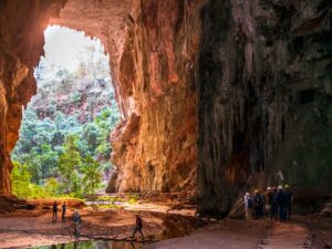 Interior de caverna enorme aberta para floresta exuberante com grupo de exploradores