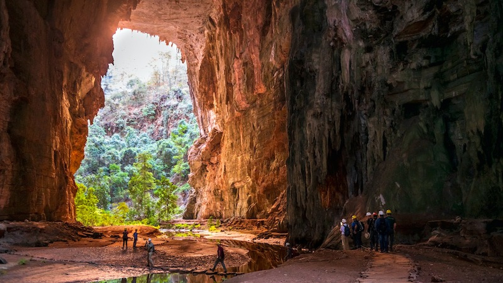 Interior de caverna enorme aberta para floresta exuberante com grupo de exploradores
